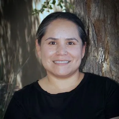 A woman in black shirt standing next to tree.