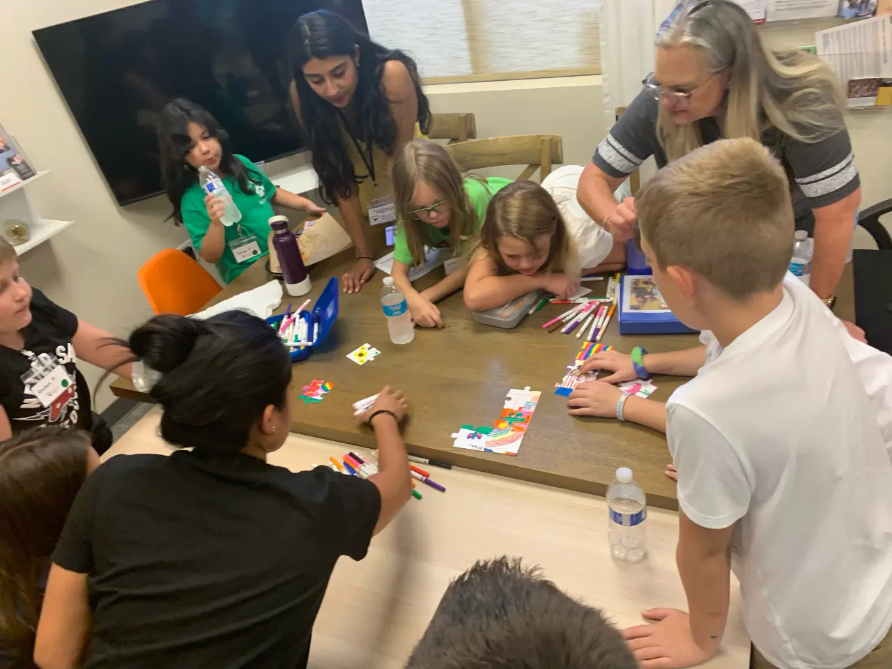 A group of children and adults around a table, engaged in a puzzle activity indoors.
