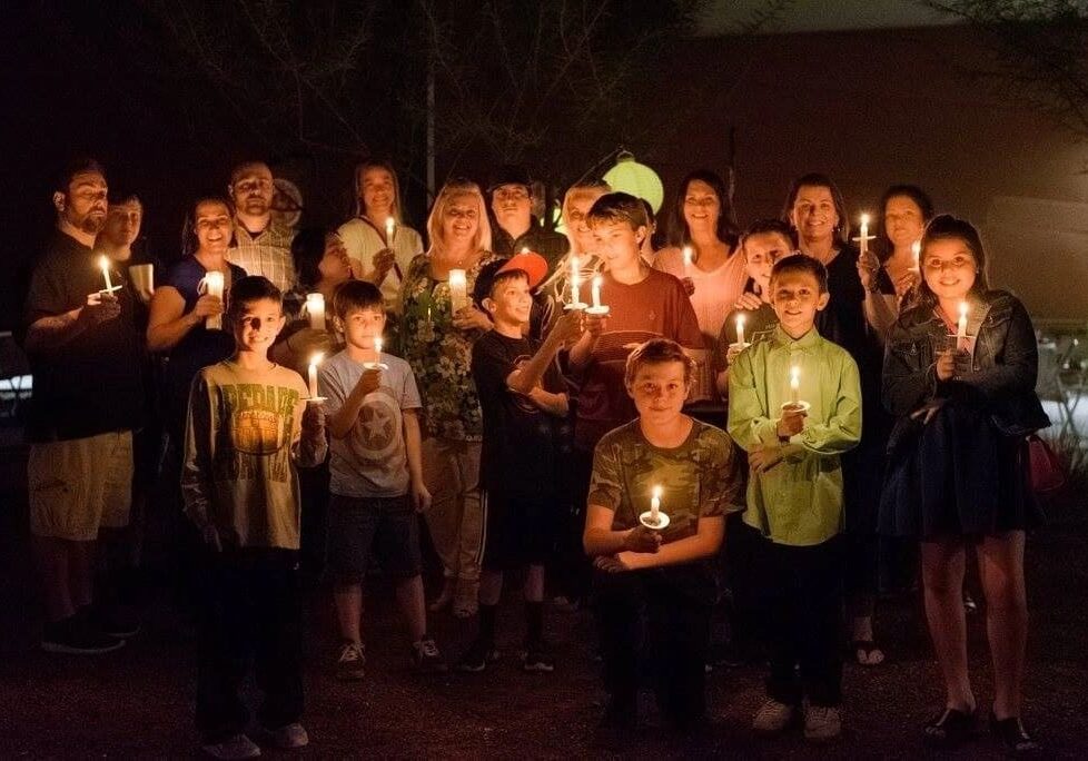 Group of people of various ages holding candles at a nighttime outdoor gathering.